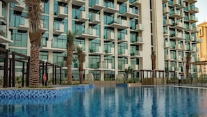A modern hotel with a pool, multiple balconies, and palm trees. - Bloomfields 1BR Azizi Farhad Burj View (Dubai)