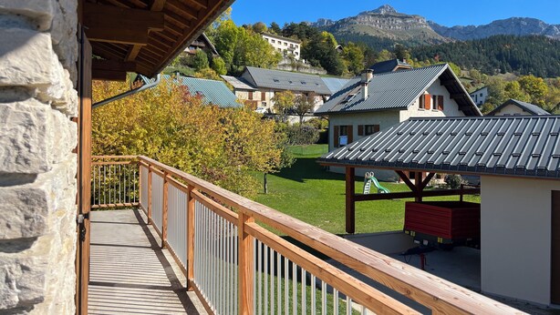 En balkon med stenvæg, trægelænder og udsigt til huse og bjerge.