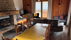 En hyggelig stue med en pejs af sten, træbjælker i loftet, et spisebord med stole og en sofa.