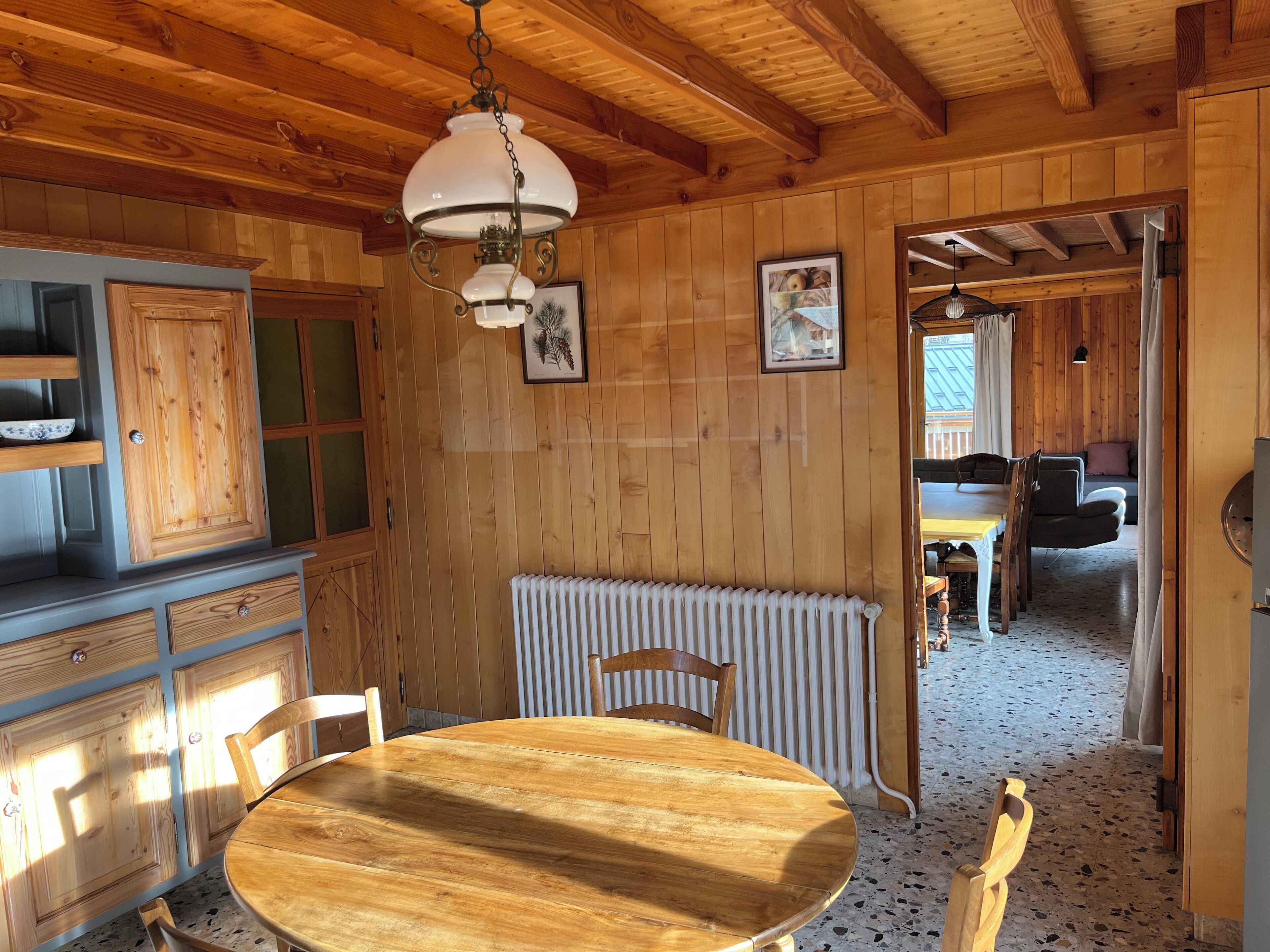 Interior em madeira com uma mesa redonda, cadeiras, radiador e luminária no teto.