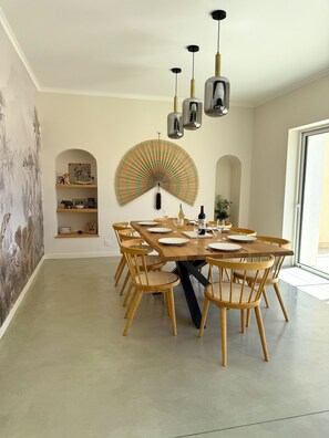 A dining area with a wooden table set for six, surrounded by wicker chairs. There are hanging pendant lights above the table, and a large fan is mounted on the wall. - Large, renovated Provençal farmhouse with a pool (Valréas)
