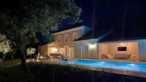 A nighttime view of a house with a swimming pool, outdoor seating, and a large tree. - Large renovated Mas provençale with swimming pool (Valréas)