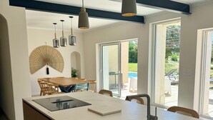 A modern kitchen with a large island, pendant lights, and a view of the outdoor patio. - Large renovated Mas provençale with swimming pool (Valréas)