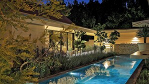 A swimming pool with a tiled edge, surrounded by lush greenery and a well-lit building. - Bel Ombre Hills, 2200m2 luxury property in upper Constantia (Cape Town)