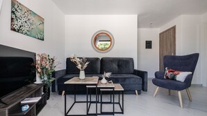 En moderne stue med en sort sofa, en blå lænestol, et sofabord, et fjernsyn og et maleri på væggen.