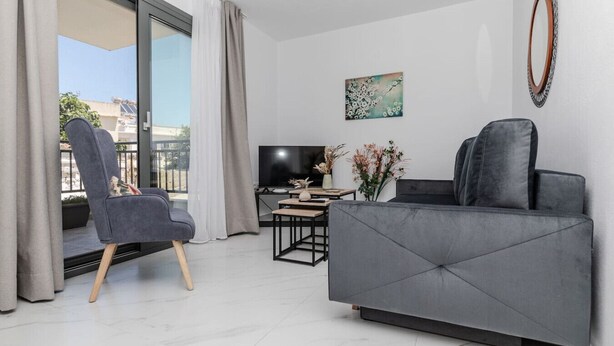 En moderne stue med en grå sofa, en grå lænestol, et fladskærms-TV og et billede på væggen.
