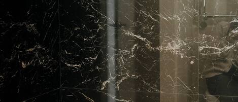 A bathroom with a black marble wall, a white sink, and two bottles of shampoo on a shelf.