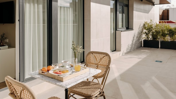 A modern outdoor dining area with a table set for breakfast, including fruits, a glass of juice, and a cup of coffee. - Hotel PAX Atocha (Madrid)