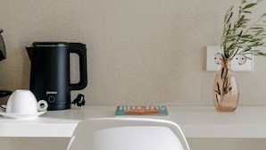 A hotel room with a white desk, a black coffee maker, a white cup, a small figurine, a book, and a vase with a plant. - Hotel PAX Atocha (Madrid)