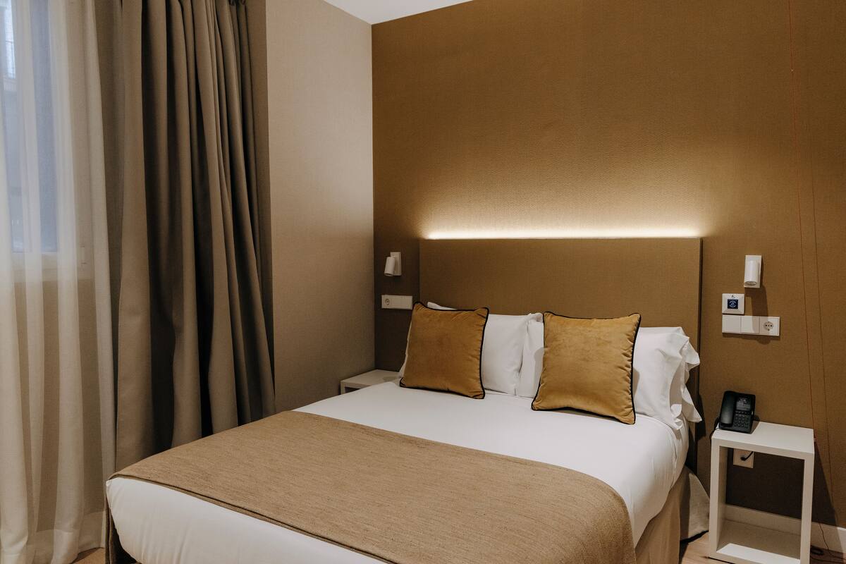 A hotel room with a large bed, a bedside table with a phone, and a wall-mounted light.