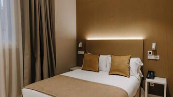 Una habitación de hotel con una cama grande, una mesita de noche con teléfono y una lámpara de pared.