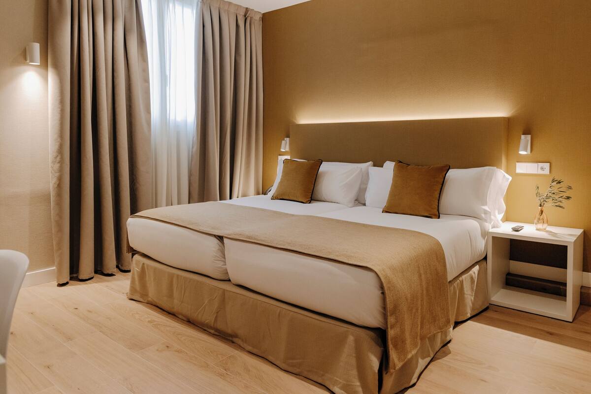 A neatly arranged hotel room with a large bed, a bedside table with a vase, and a chair.
