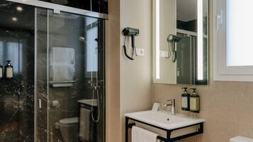 Un baño moderno con ducha envuelta en vidrio, lavamanos blanco y un espejo grande.