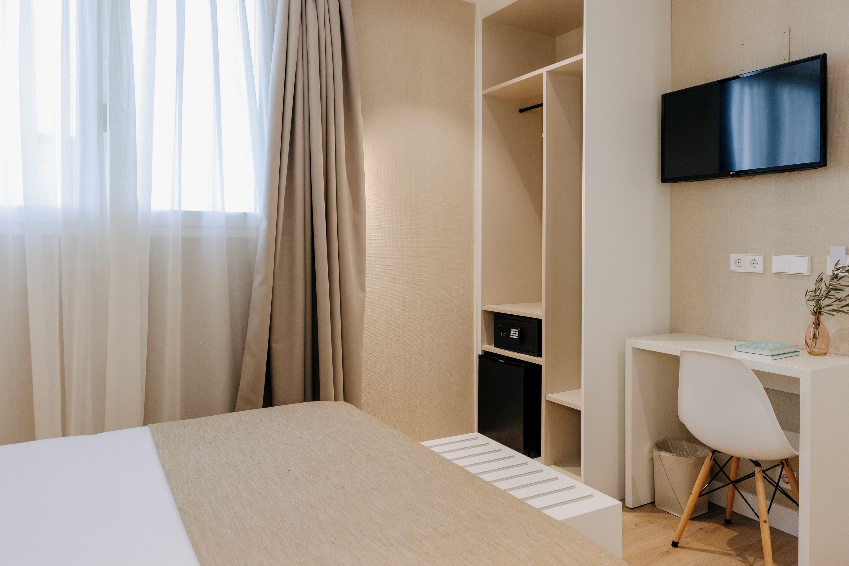 Quarto de hotel com uma cama, uma escrivaninha, uma cadeira, uma televisão e um guarda-roupa.