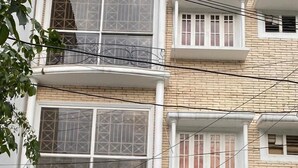 A multi-story residential building with a brick facade, white window frames, and a black metal gate. - Mithra Homes (Hyderabad)