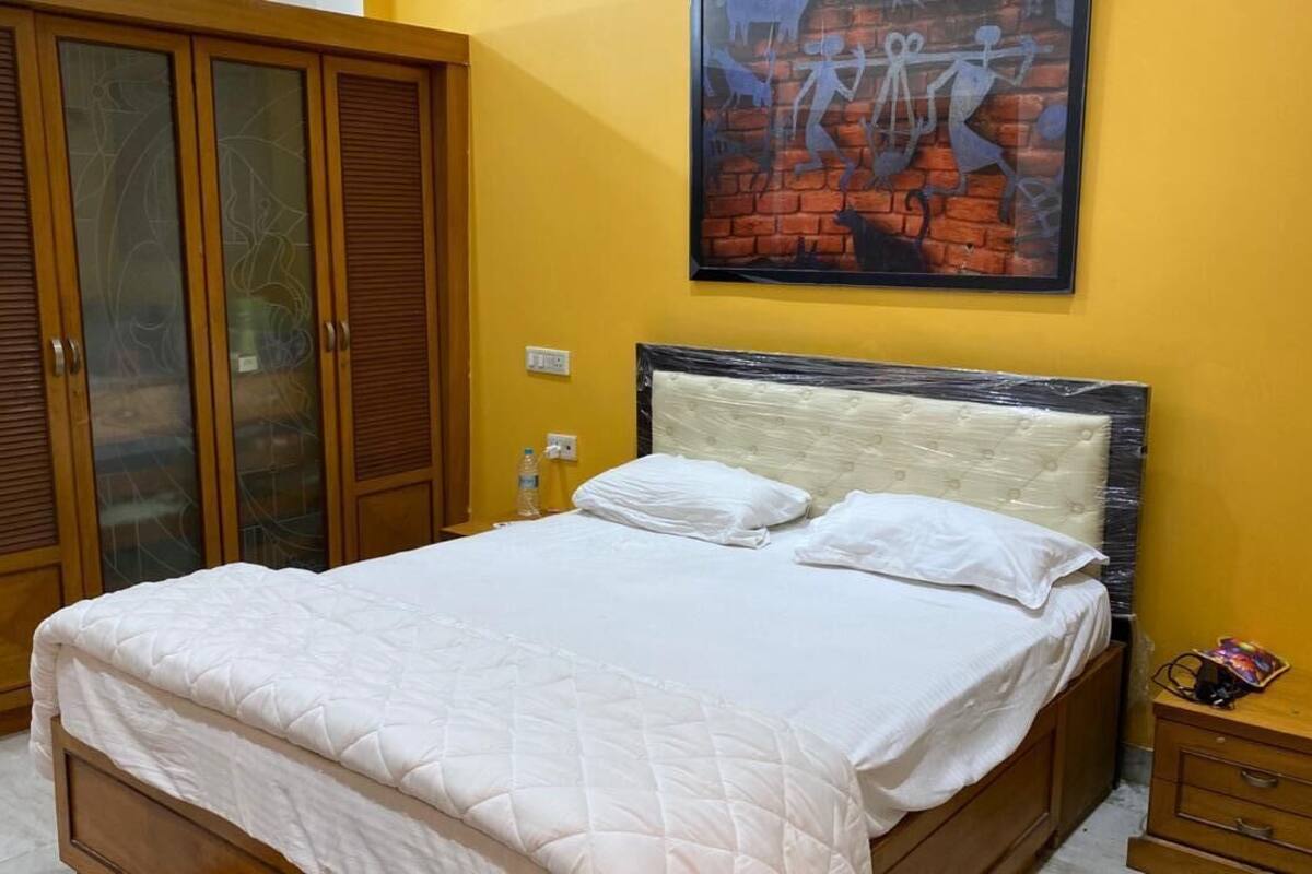 A bedroom with a bed, wooden wardrobe, and a painting on the wall.