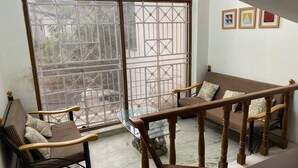A room with a sofa, a wooden chair, a glass table, and a staircase. - Mithra Homes (Hyderabad)