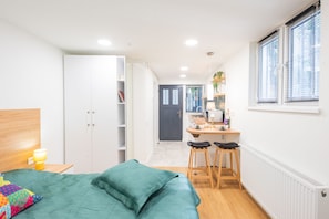 A bedroom with a bed, a desk, and a chair. There is a wardrobe, a radiator, and a window with blinds. - HB apartments Irakli Abashidze (Tbilisi)