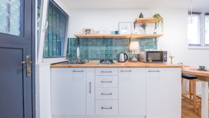 A modern kitchen with white cabinets, a wooden countertop, a microwave, a kettle, and a window with blinds. - HB apartments Irakli Abashidze (Tbilisi)