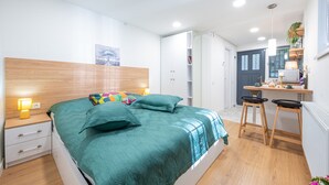 A modern bedroom with a wooden headboard, a bed with a teal bedspread, a bedside table with a lamp, and a small desk with stools. - HB apartments Irakli Abashidze (Tbilisi)