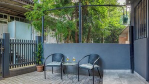 An outdoor seating area with two chairs and a table, a potted plant, and a view of trees and a building in the background. - HB apartments Irakli Abashidze (Tbilisi)