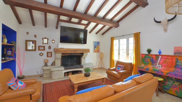 A living room with a fireplace, leather sofas, a television, and a colorful cabinet. - Les Salines holiday home 5 minutes from the beach (Le Grau-du-Roi)