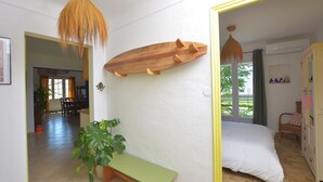 A bedroom with a bed, a wooden shelf, a bench, and a hanging light fixture. - Les Salines holiday home 5 minutes from the beach (Le Grau-du-Roi)