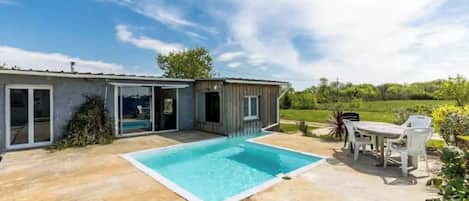 Una casa con piscina, un patio con mesa y sillas, y un jardín.
