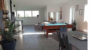 Ein geräumiger Wohnbereich mit Billardtisch, einem Esstisch mit Stühlen und einer Küchenzeile mit Herd und Schränken.