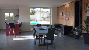 Ein geräumiger Wohnbereich mit Esstisch, Stühlen, einer Couch und einem großen Fenster mit Blick auf einen Swimmingpool.