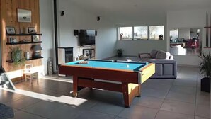 Ein modernes Wohnzimmer mit einem Billardtisch, einer Couch und einem Fernseher.