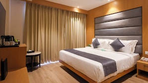 A modern hotel room with a large bed, a bedside table, a desk, and a ceiling fan. - Click Hotel Bhuntar,Kullu-Bhuntar Airport (Aut)