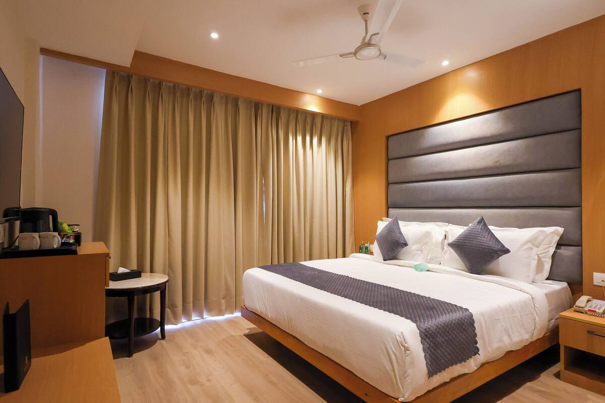 A modern hotel room with a large bed, a bedside table, a desk, and a ceiling fan.