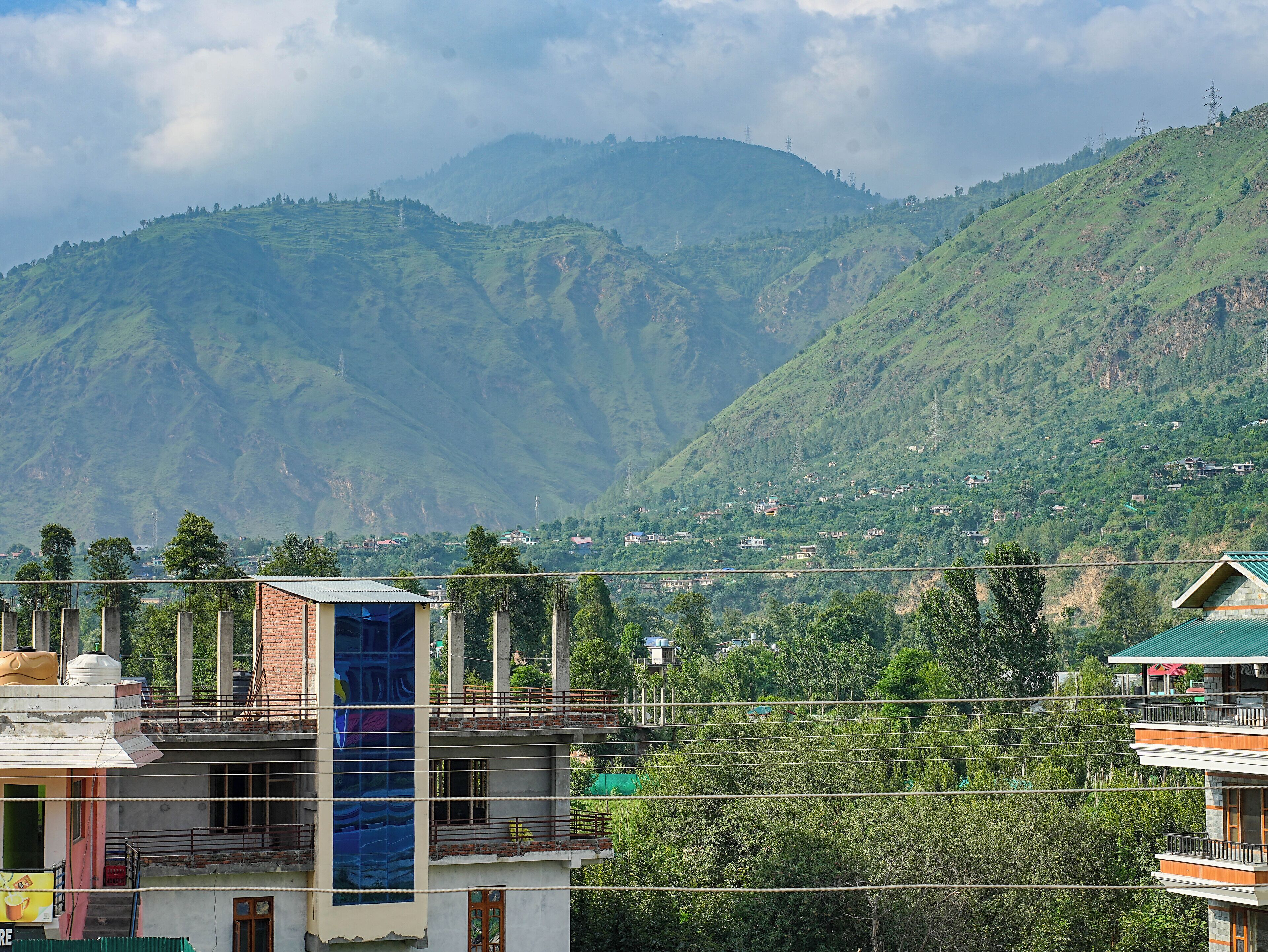 A multi-story building with a prominent blue glass facade, surrounded by lush green hills and scattered houses.