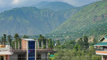 A multi-story building with a prominent blue glass facade, surrounded by lush green hills and scattered houses.