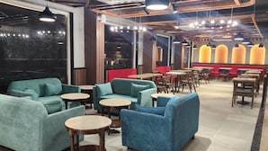 A modern restaurant interior with teal sofas, wooden tables, and pendant lighting. - Click Hotel Bhuntar,Kullu-Bhuntar Airport (Aut)