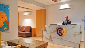 A hotel reception area with a marble reception desk, a sofa, a wooden table, and a map on the wall. - Click Hotel Bhuntar,Kullu-Bhuntar Airport (Aut)
