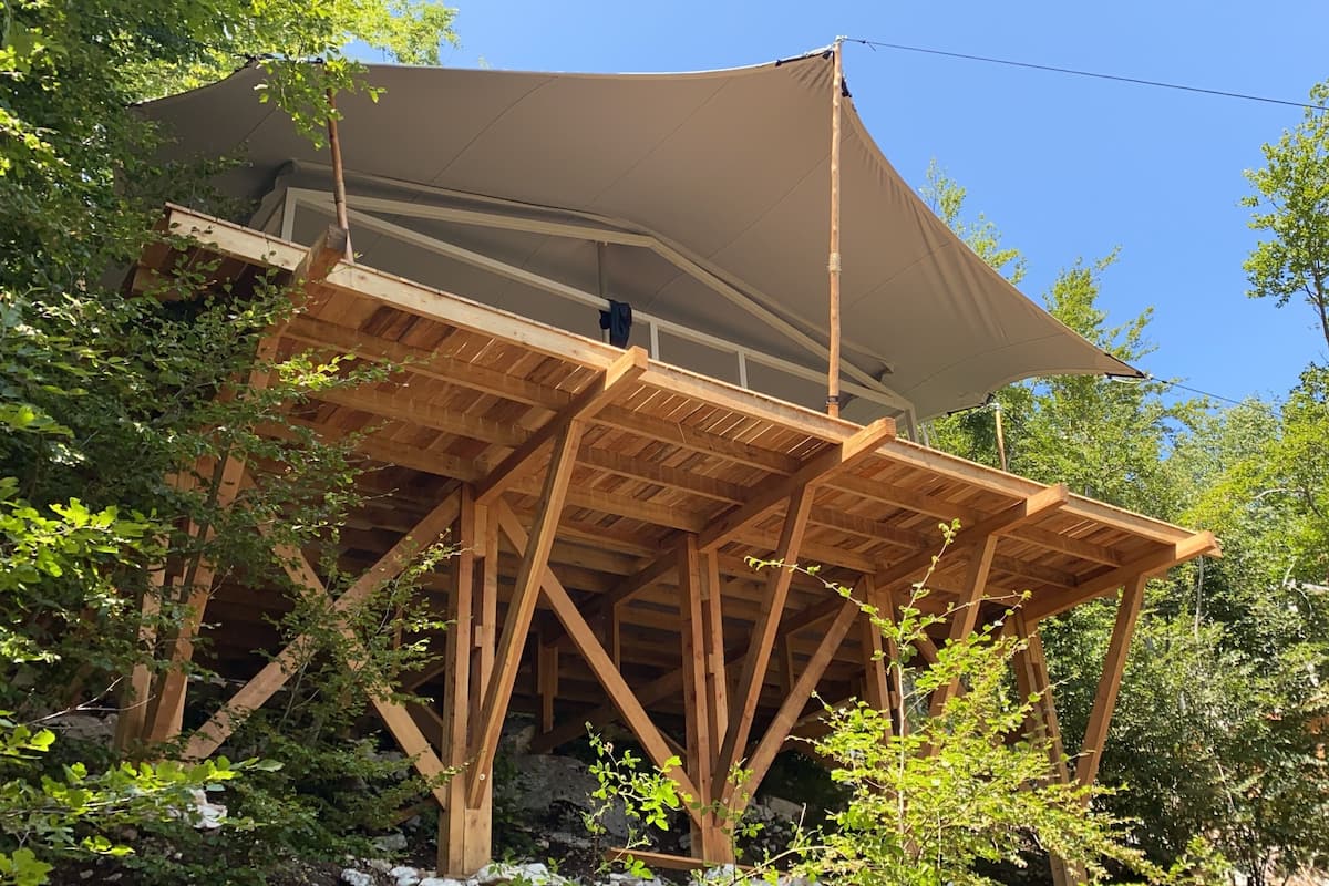 Une structure de terrasse en bois, dotée d’un grand auvent et entourée d’arbres.