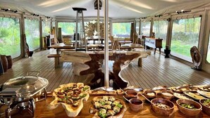 A dining area with a central wooden table, surrounded by wooden chairs, and a buffet setup with various dishes and bowls. - Ashuma retreat center (Cetinje)