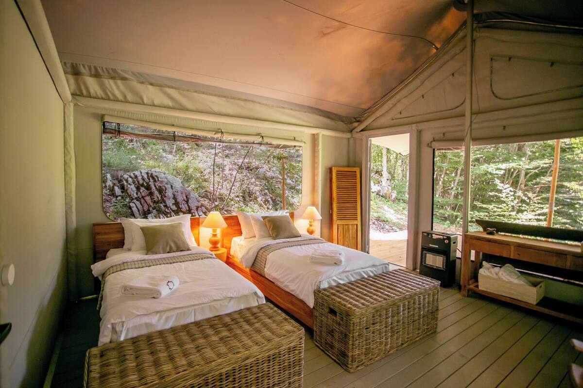 Une chambre avec deux lits, des paniers en osier, une table en bois et une vue sur la verdure environnante.
