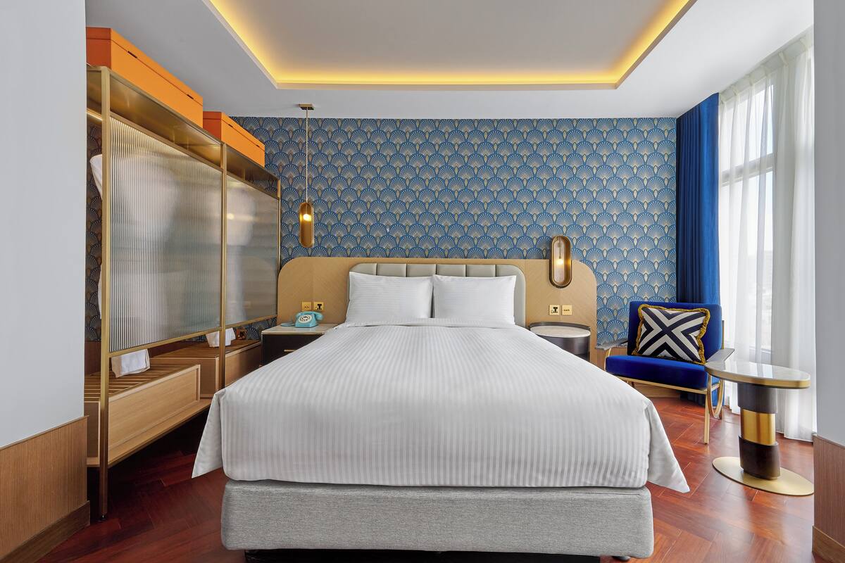 A hotel room with a large bed, a wardrobe, a bedside table, a chair, and a nightstand.
