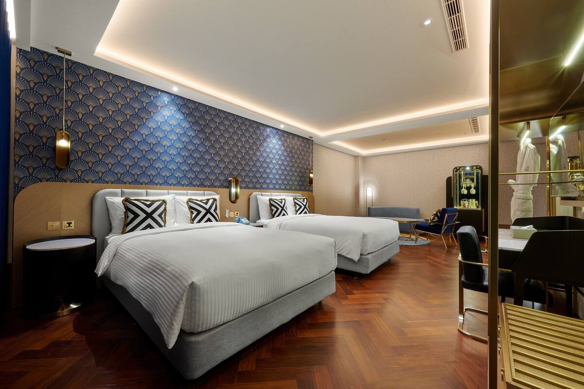 A hotel room with two beds, a sitting area, and a mirror.