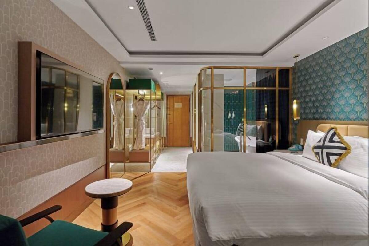 A modern hotel room with a large bed, a seating area, and a glass-enclosed bathroom.