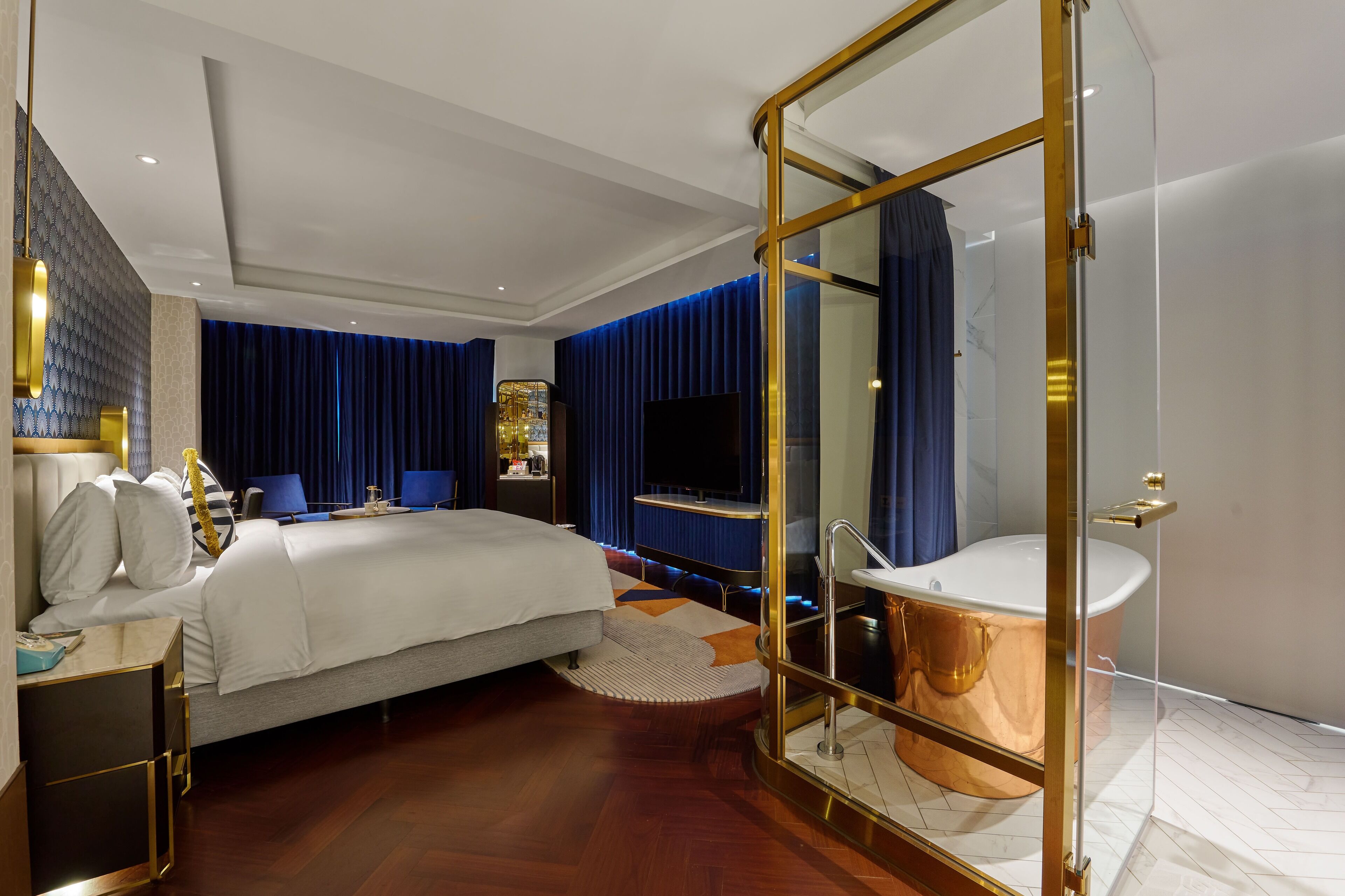 Una habitación de hotel moderna con una cama grande, un baño con paredes de cristal y un televisor.