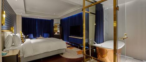 Una habitación de hotel moderna con una cama grande, un baño con paredes de cristal y un televisor.