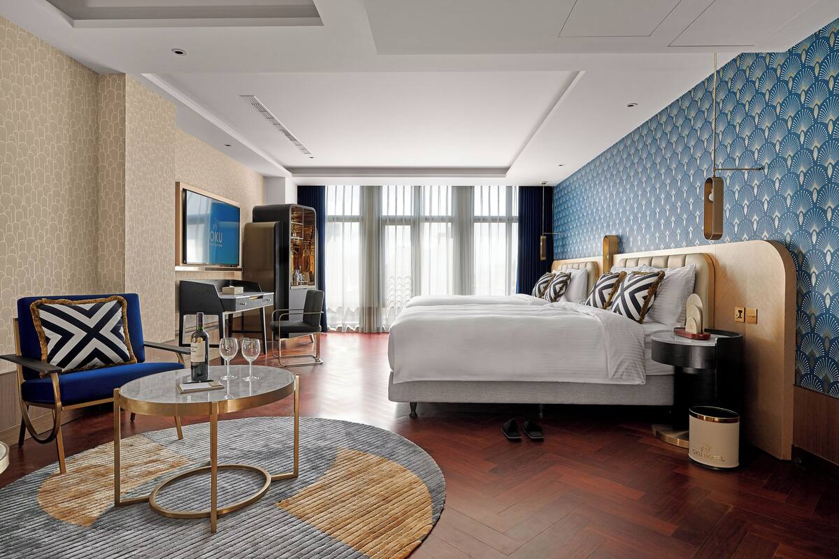 A hotel room with a bed, a sofa, a TV, a desk, and a window with curtains.