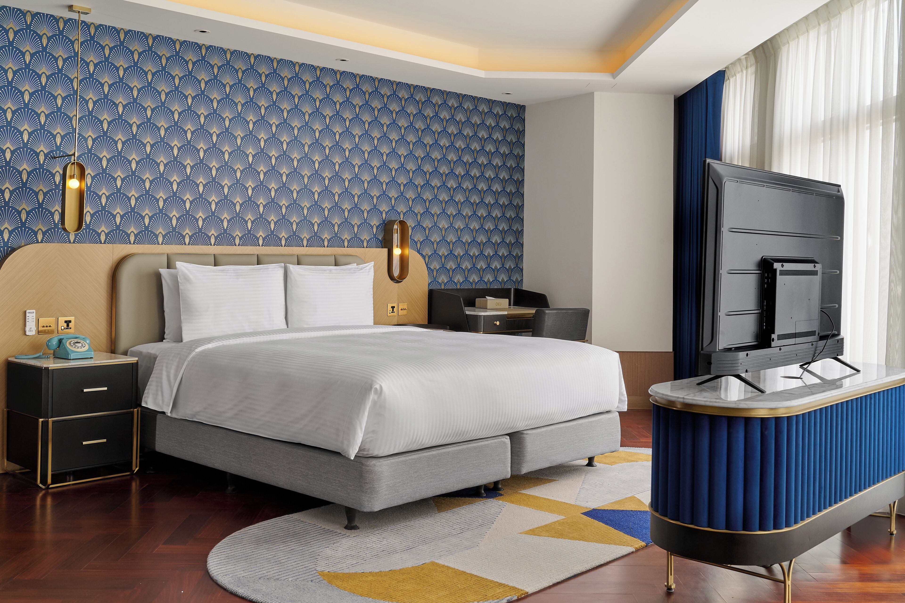 Une chambre d’hôtel moderne avec un grand lit, une télévision, un bureau et un papier peint à motifs.