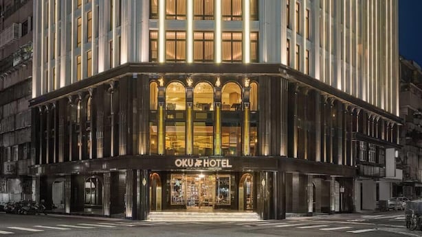 Un hotel de estilo arquitectónico clásico, con una entrada destacada que cuenta con amplios ventanales en arco y un cartel sobre la entrada.