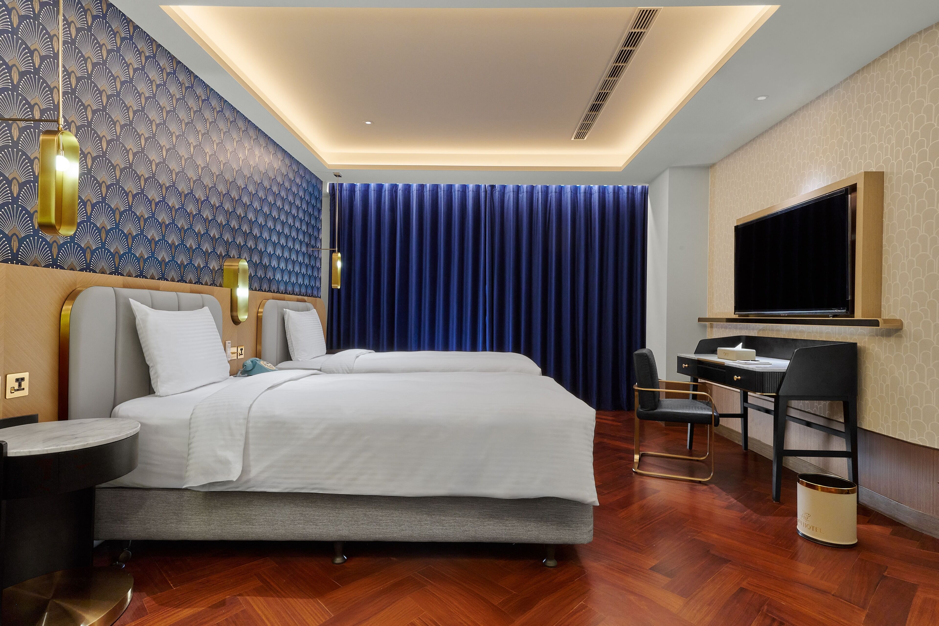 A modern hotel room with a large bed, a desk with a chair, a TV, and a patterned wall.
