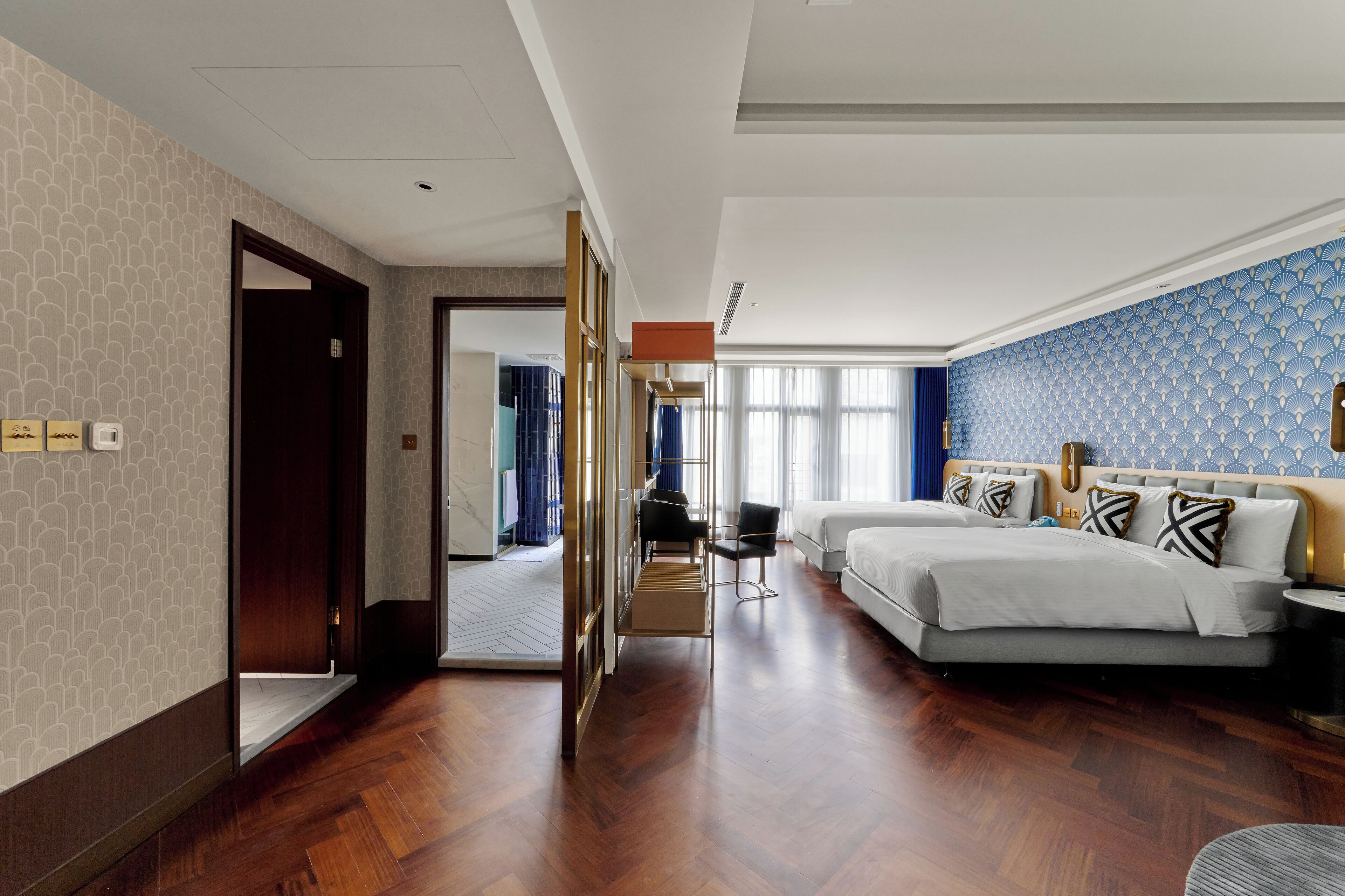 Habitación de hotel con una cama grande, un escritorio y una silla. Hay una puerta que conduce a otra habitación.